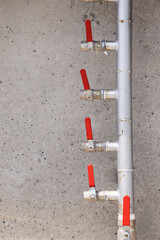 Metal pipe with multiple red shut off valves fixed to a concrete wall, ensuring controlled water...