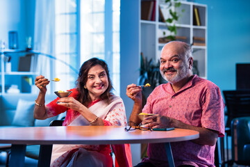 Old Indian couple eating ice cream sitting together and enjoying sweet moment indoors