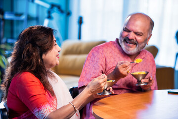 Old Indian couple eating ice cream sitting together and enjoying sweet moment indoors