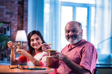 Old Indian couple eating ice cream sitting together and enjoying sweet moment indoors