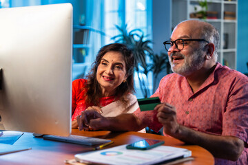 Elderly Indian couple making online payment using credit card and laptop at home