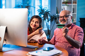 Fototapeta premium Elderly Indian couple making online payment using credit card and laptop at home