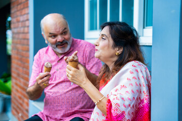 Asian elderly couple happily enjoying ice cream together outside on a warm sunny day