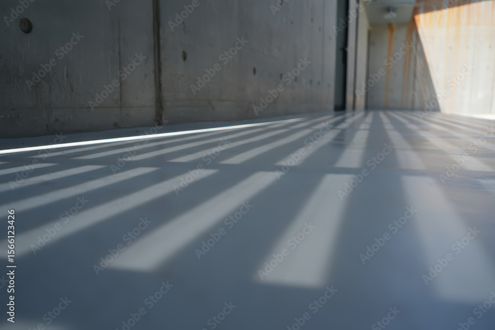 Poster shadows cast on a concrete floor in a building with concrete walls and a light source on the right