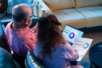 Senior Indian couple working on monthly finances together using laptop and documents at home