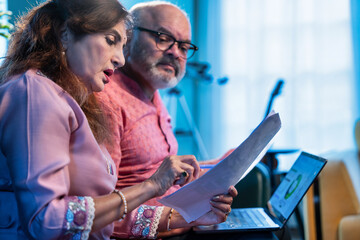 Senior Indian couple working on monthly finances together using laptop and documents at home