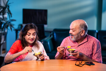 Old Indian couple eating ice cream sitting together and enjoying sweet moment indoors