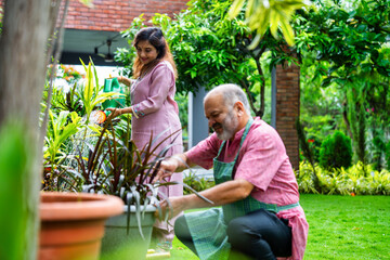 Retired Indian couple watering plants together in home garden, enjoying peaceful morning activity