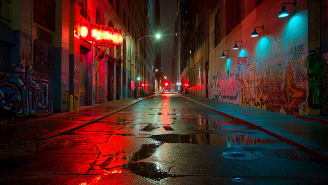 Moody urban alleyway at night, graffiti, red and blue neon lights, wet asphalt.