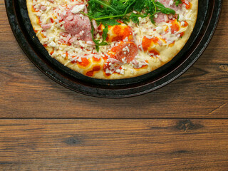 A pizza with ham and spinach on a black tray. The pizza is sitting on a wooden table. Fine Italian...