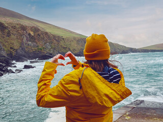 Girl tourist in yellow jacket and hat explore stunning Dunquin Pier area in county Kerry, Ireland....
