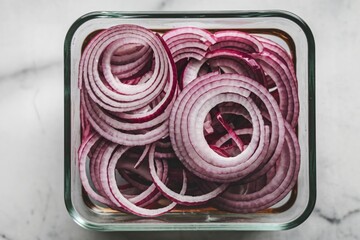A photo of a transparent glass container with thinly sliced red onions