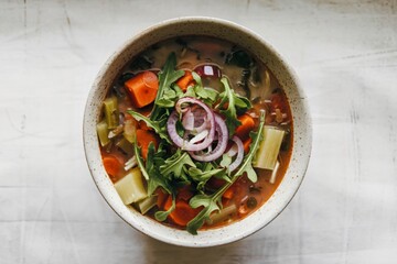 A photo of a top view of a vegetable soup garnished with sliced shallots
