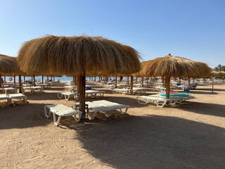 Sun loungers under thatched beach umbrellas on the beach overlooking the sea coast and blue sky