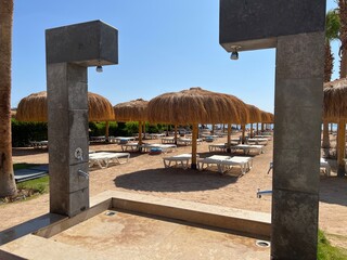 Shower on the beach, in the background sun loungers under thatched beach umbrellas on the beach with a view of the sea coast and blue sky