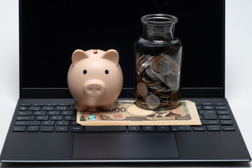 パソコンの上に置かれたお金と豚の貯金箱