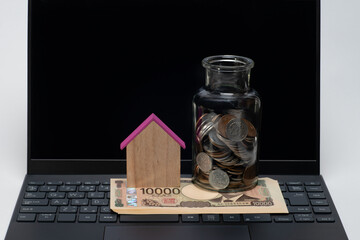 ノートパソコンと一万円札と家型の模型と瓶に入った小銭