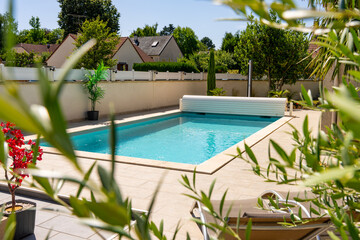 Piscine privée avec margelles en pierre beige, entourée de verdure et équipée d’un rouleau pour bâche, dans un jardin paysager.