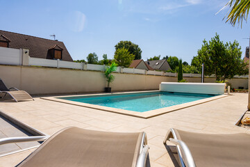 Piscine privée avec margelles en pierre beige, entourée de verdure et équipée d’un rouleau pour bâche, dans un jardin paysager.
