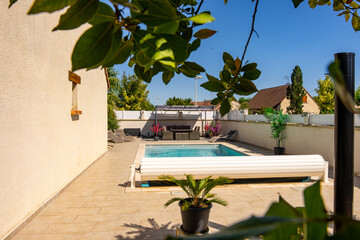 Piscine privée avec margelles en pierre beige, entourée de verdure et équipée d’un rouleau...