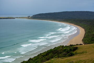Curved Beach with Gentle Waves and Lush Greenery