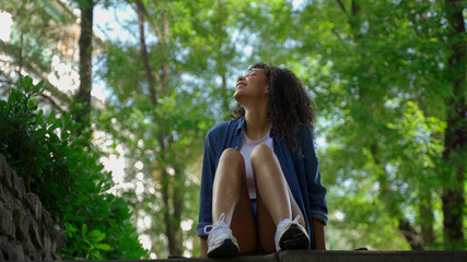 Carefree female skater resting on a stone bench in a lush green park, embracing the tranquility of nature