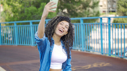 Happy stylish woman taking a selfie with her smartphone while sitting on a skateboard on a bridge