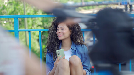 Young woman using mobile phone while sitting on skateboard on city bridge