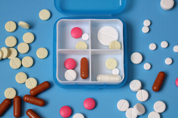 Daily pill organizer box surrounded by assorted pills on blue background