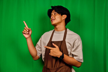 Young Man Wearing Casual Clothes and Apron Pointing Up Against Green Screen