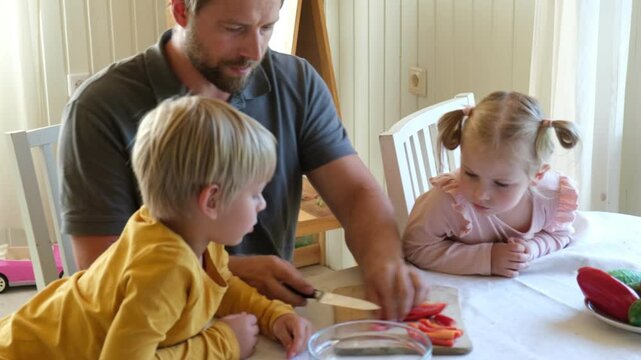 Young father with a toddlers cooking. Daughter and son cutting vegetables, preparing healthy food in kitchen. Daddy relaxing and spending time with his kids, girl and boy together at home. Family life