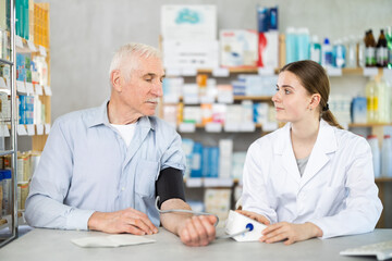 Young female pharmacist measuring blood pressure of mature man
