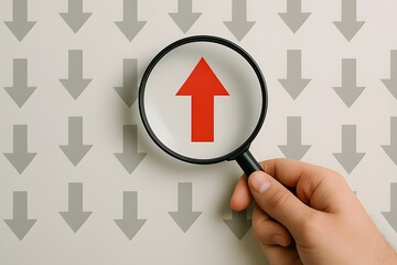 Magnifying glass focuses on a single red upward arrow amidst many gray downward arrows