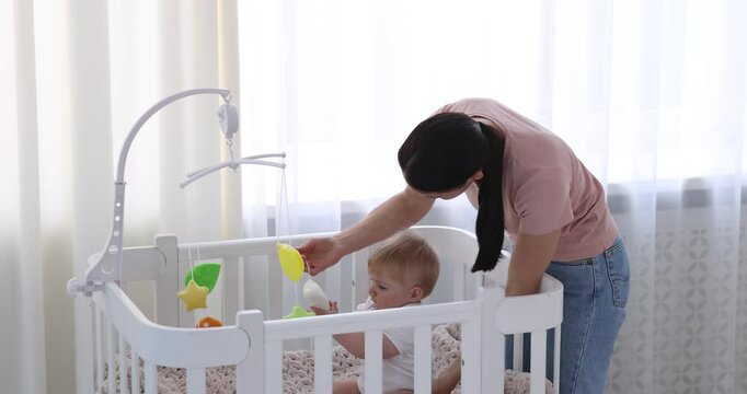 Mother putting her little baby into crib at home