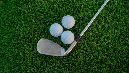 Golf clubs and golf balls on a green lawn in a beautiful golf course with morning sunshine.