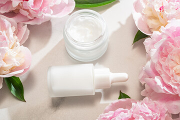 Skincare product display with cream jar, serum bottle and peony accent, ideal for e-commerce...