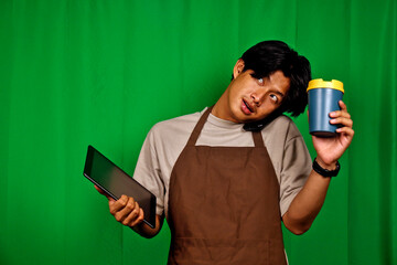 Young Man Wearing Apron Holding Coffee Cup and Digital Tablet Standing in Front of Green Screen