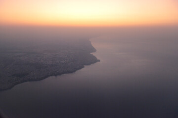 Sunrise aerial view of coastal cityscape with light morning fog and calm water