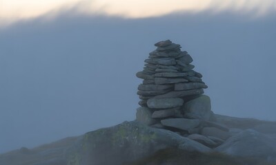 Ancient Stone Cairn on a Misty Mountain Summit: A Serene Trail Marker Shrouded in Atmospheric Fog and Haze