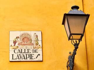 Street sign or nameplate for Calle of Lavapies on a yellow background next to a streetlight