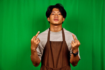 Young Man Wearing Apron Standing in Front of Green Screen Making Defiant Gesture
