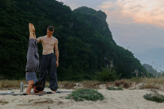 Caucasian adults practicing yoga in nature: headstand and supportive instructor