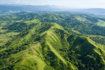 Fototapeta premium Expansive aerial view of steep green mountains under clear blue sky in a lush landscape, Aerial view of steep green mountains under clear sky