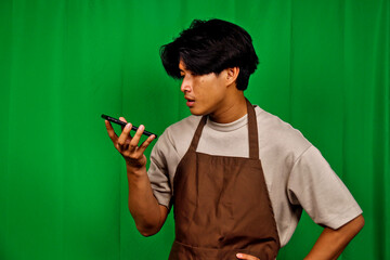 Young Male Worker Wearing Brown Apron Using Smartphone in Green Screen Studio