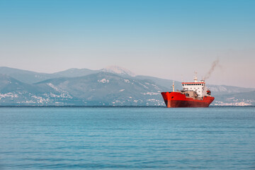 Cargo ship sailing on calm sea at sunset with mountains in background, maritime transport concept