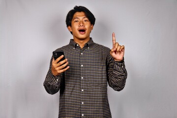 Young Man Wearing Checked Shirt Using Smartphone Pointing Up in Surprised Expression