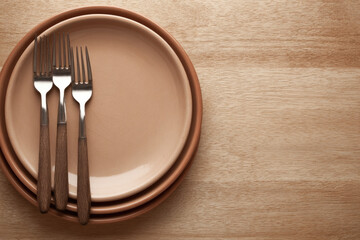 Three metal forks with wooden handles rest on stacked ceramic plates, warm brown tones, minimalist table setting, top view, inviting and calm dining atmosphere