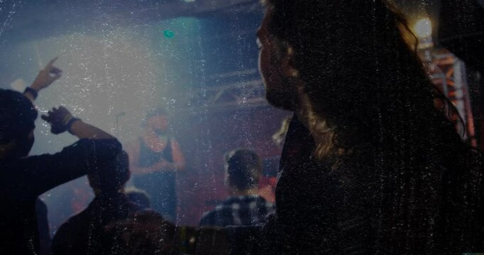 Long-haired fan raising arms toward pulsing spotlights triggered by music beat across concert stage