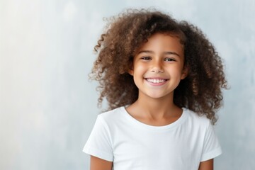 Happy child with beautiful curly hair smiling, showing perfect white teeth, in front of light blue background