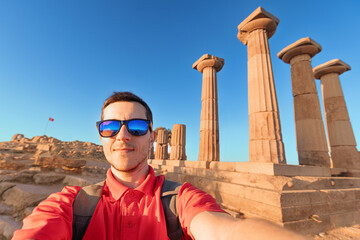 Male tourist capturing a selfie in front of ancient Greek columns at the Temple of Athena in Assos,...